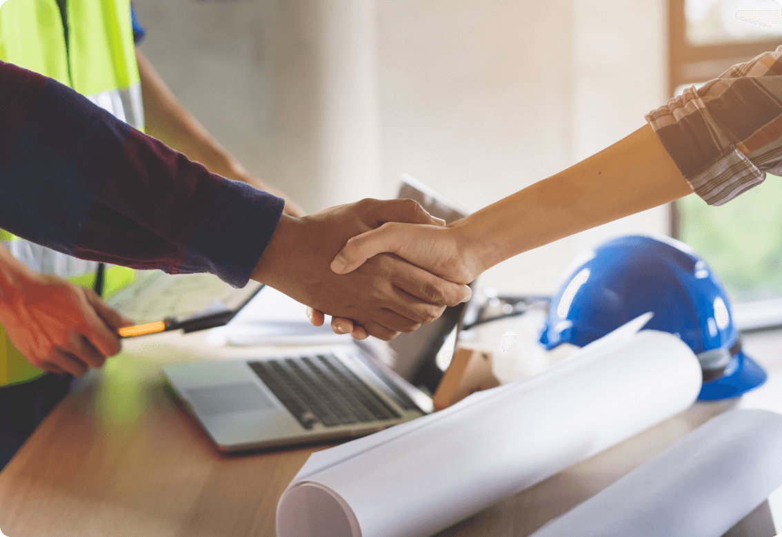 Two hands shaking hands over table has construction plans